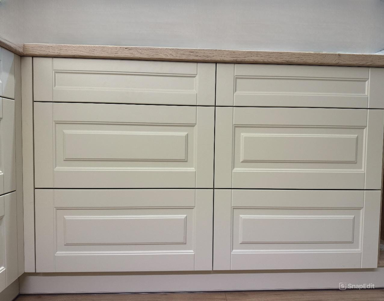 Fronty szuflad w zabudowie kuchennej, kremowe, z frezowanymi ramkami, drewniany blat, widok z bliska.