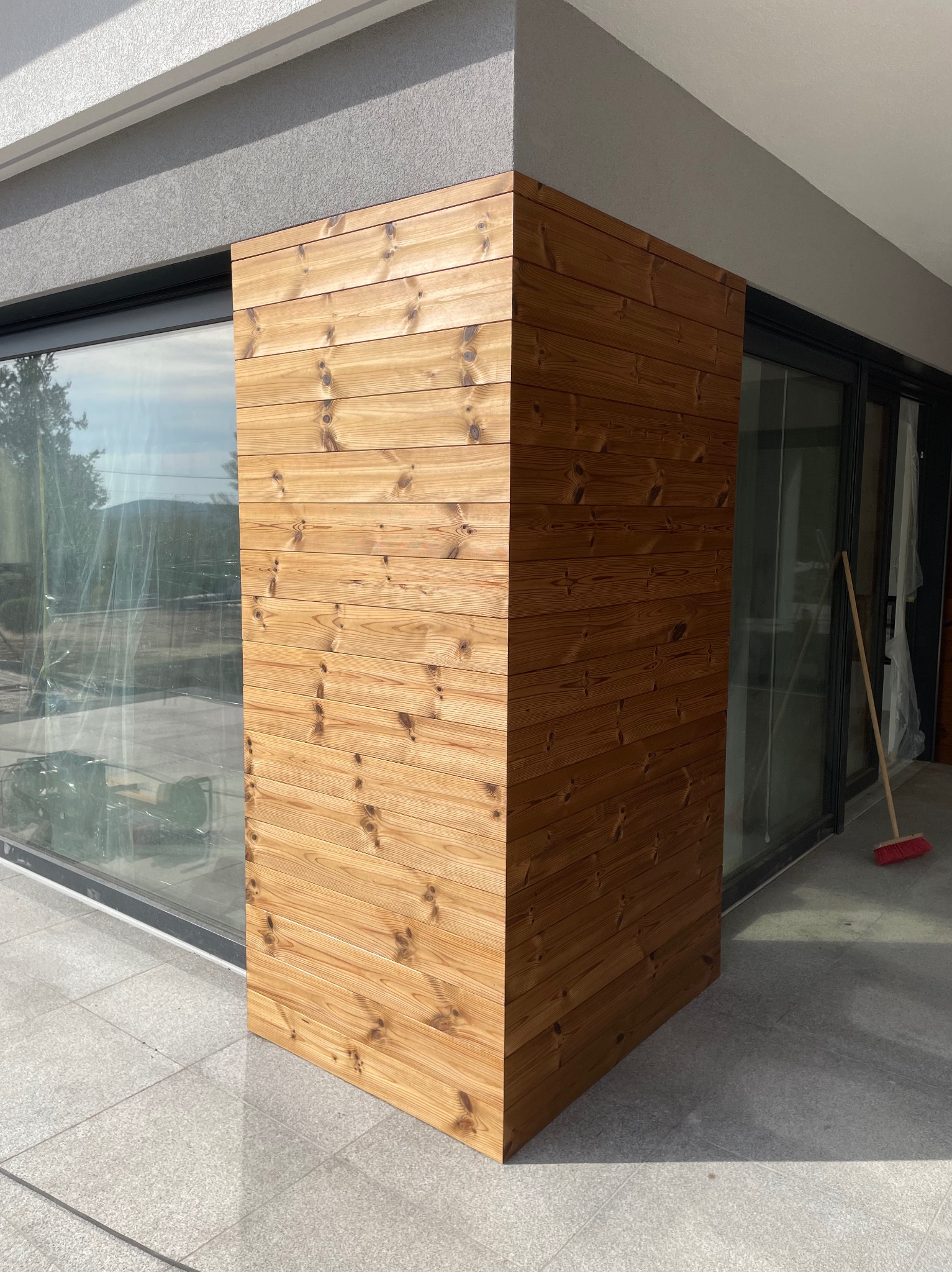 Wykończony narożnik tarasu z desek drewnianych, przylegający do okna tarasowego i ściany budynku, widoczna zamiatarka.