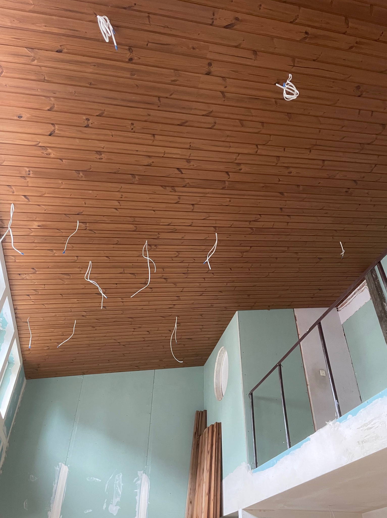 Wnętrze w trakcie wykańczania: drewniana boazeria na suficie z wystającymi kablami elektrycznymi, ściany pokryte płytami gipsowo-kartonowymi w kolorze miętowym, widoczne elementy konstrukcyjne...