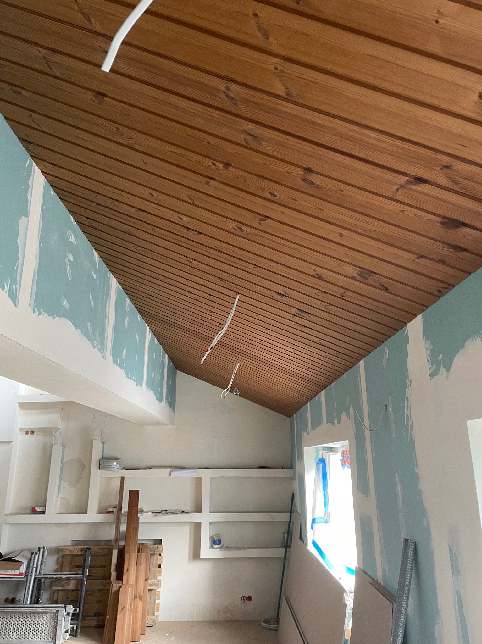 Wnętrze w trakcie remontu: sufit wykończony boazerią, ściany przygotowane pod malowanie, widoczne płyty gipsowe i metalowe profile.