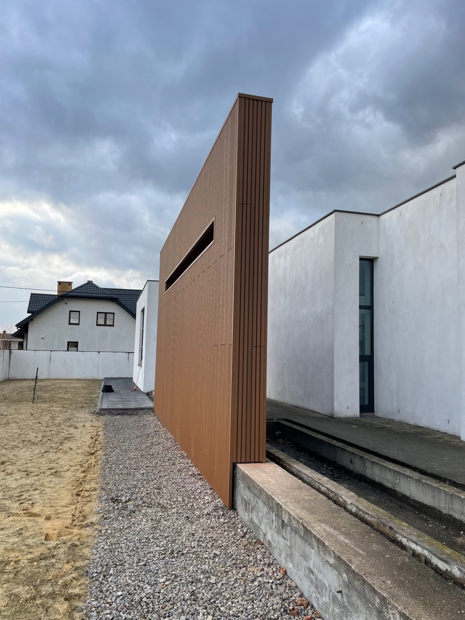 Nowoczesny dom z elementami drewnopodobnymi na elewacji i minimalistycznym oknem, widok z zewnątrz w pochmurny dzień.
