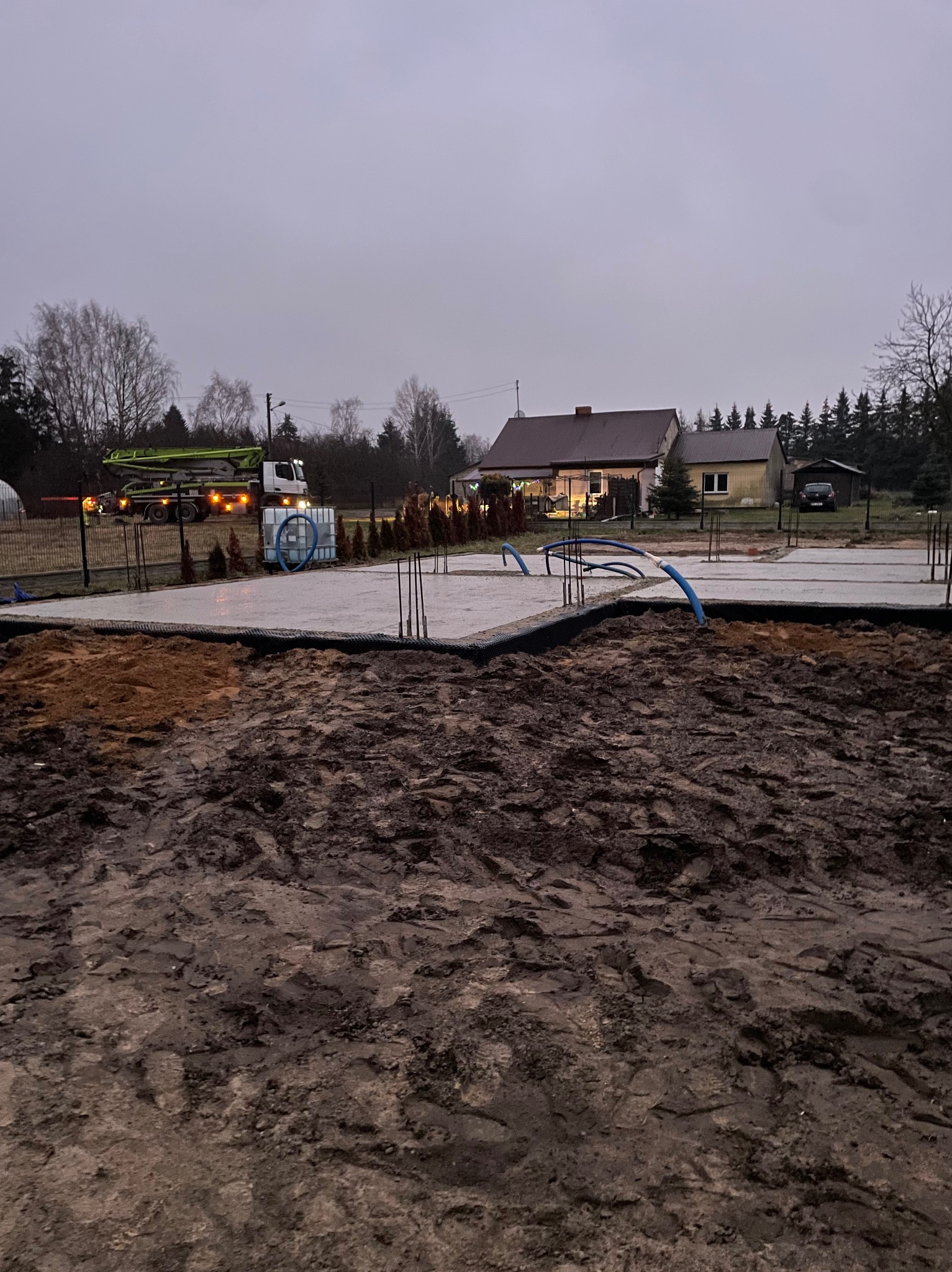 Wylany fundament pod budowę domu jednorodzinnego, widoczna pompa do betonu na działce i wystające pręty zbrojeniowe.