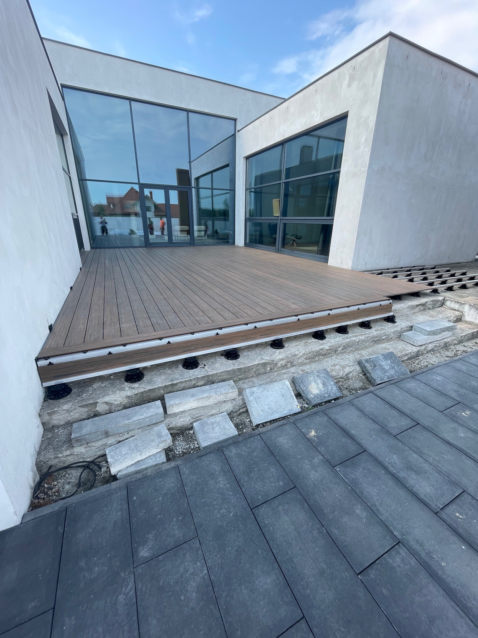 Montaż tarasu kompozytowego przy nowoczesnym domu z dużymi oknami. Widoczne elementy konstrukcyjne i częściowo ułożona nawierzchnia z desek kompozytowych.