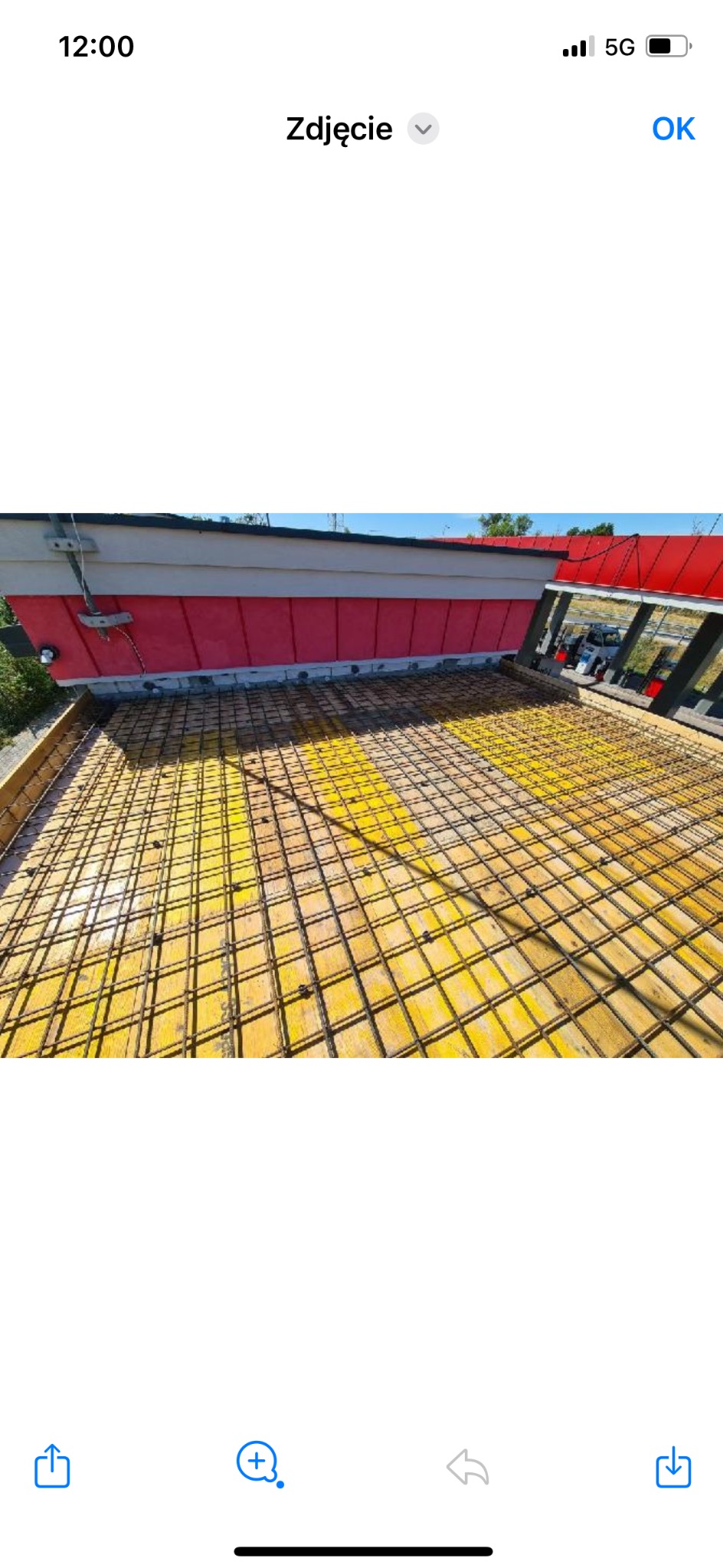 Zbrojenie fundamentu na żółtym szalunku, widok z góry. Na drugim planie fragment budynku z czerwonymi elementami. Etap budowy domu.