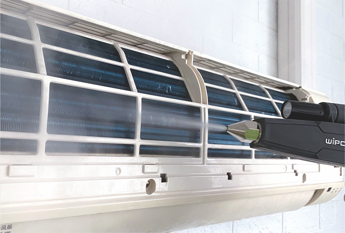 Czyszczenie parowe wnętrza klimatyzatora ściennego z widocznymi lamelami parownika, z użyciem czarnego urządzenia WIPCOOL.