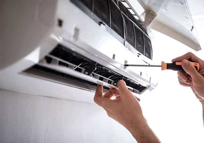 Serwisant w trakcie demontażu obudowy klimatyzatora ściennego za pomocą śrubokręta z pomarańczowo-czarną rączką, widoczne filtry i żaluzje.