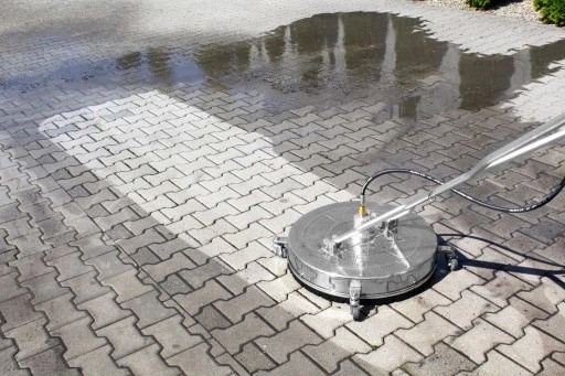 Czyszczenie kostki brukowej za pomocą okrągłej myjki ciśnieniowej; widoczna różnica w czystości między umytą a nieumytą powierzchnią.