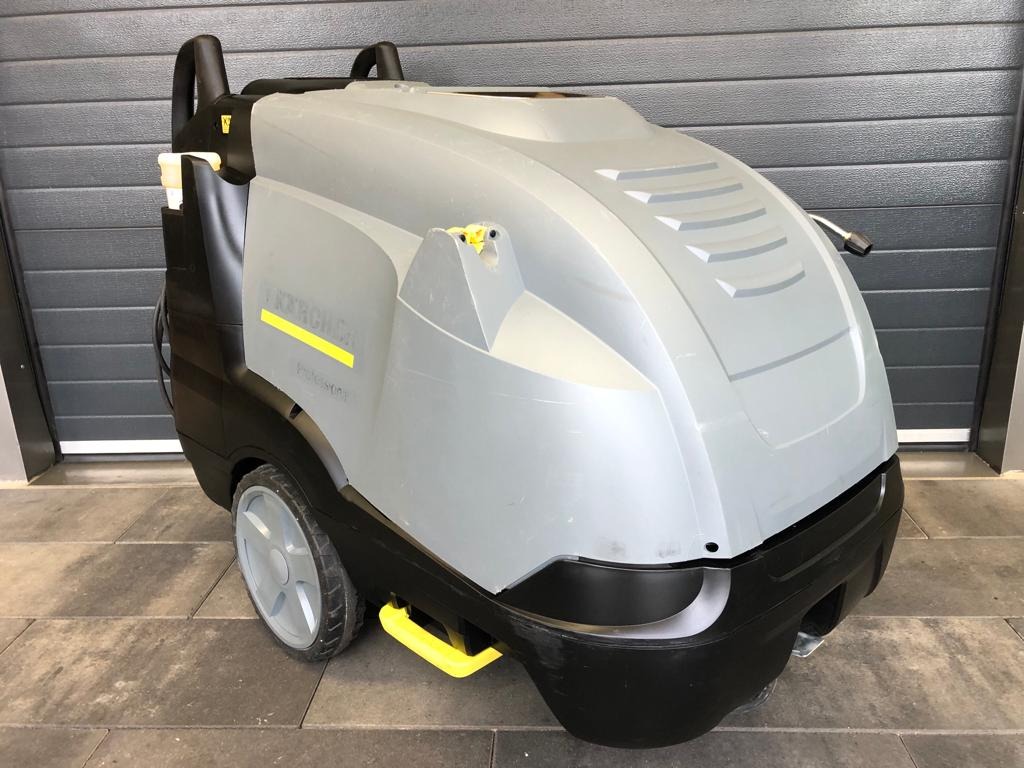 Profesjonalna myjka ciśnieniowa Karcher na kółkach, stojąca na szarym bruku, z szarą bramą garażową w tle.