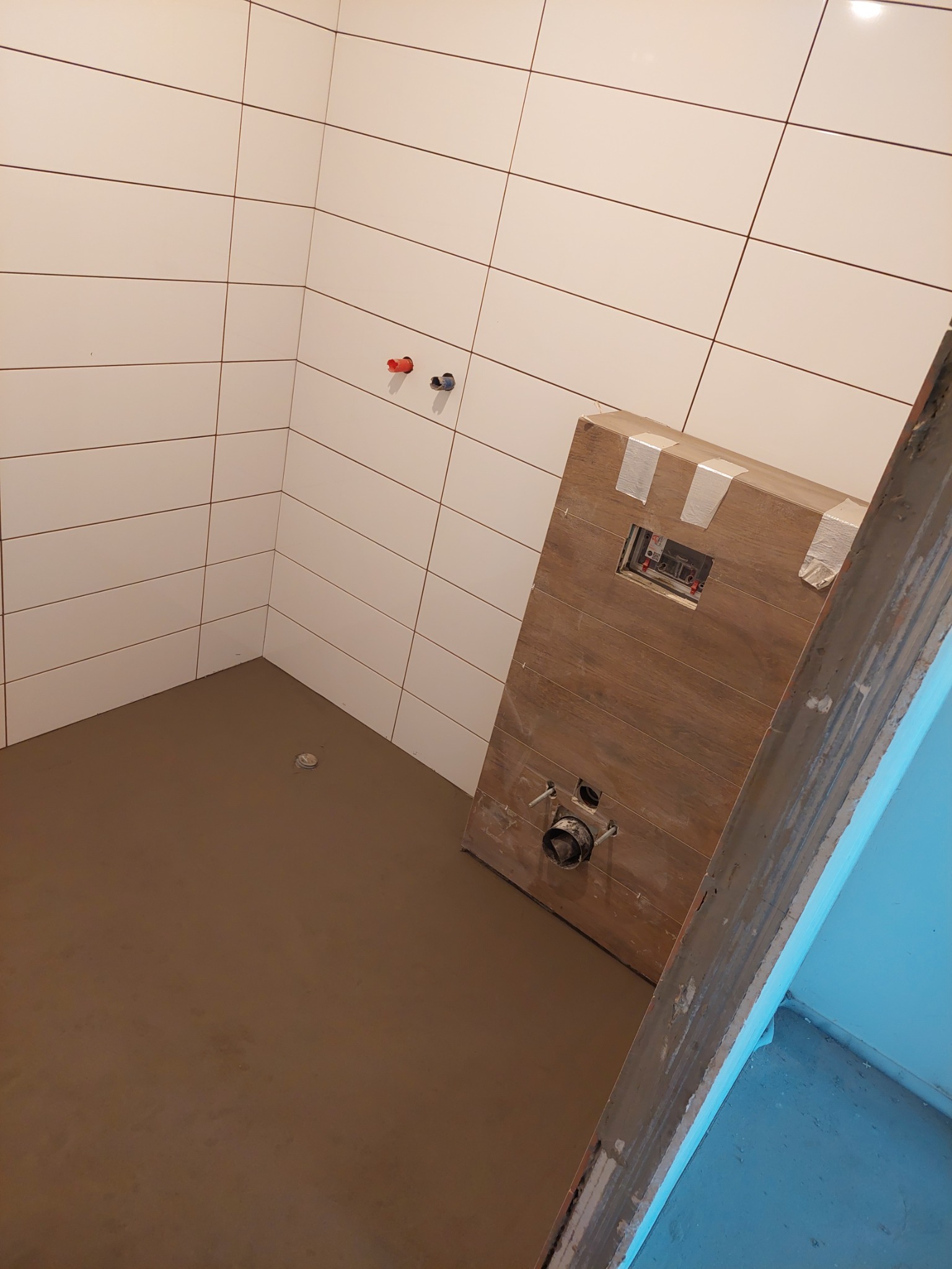 Przygotowanie łazienki do montażu toalety: wylewka podłogowa, białe płytki na ścianach, zabudowa stelaża podtynkowego z ukrytą instalacją.