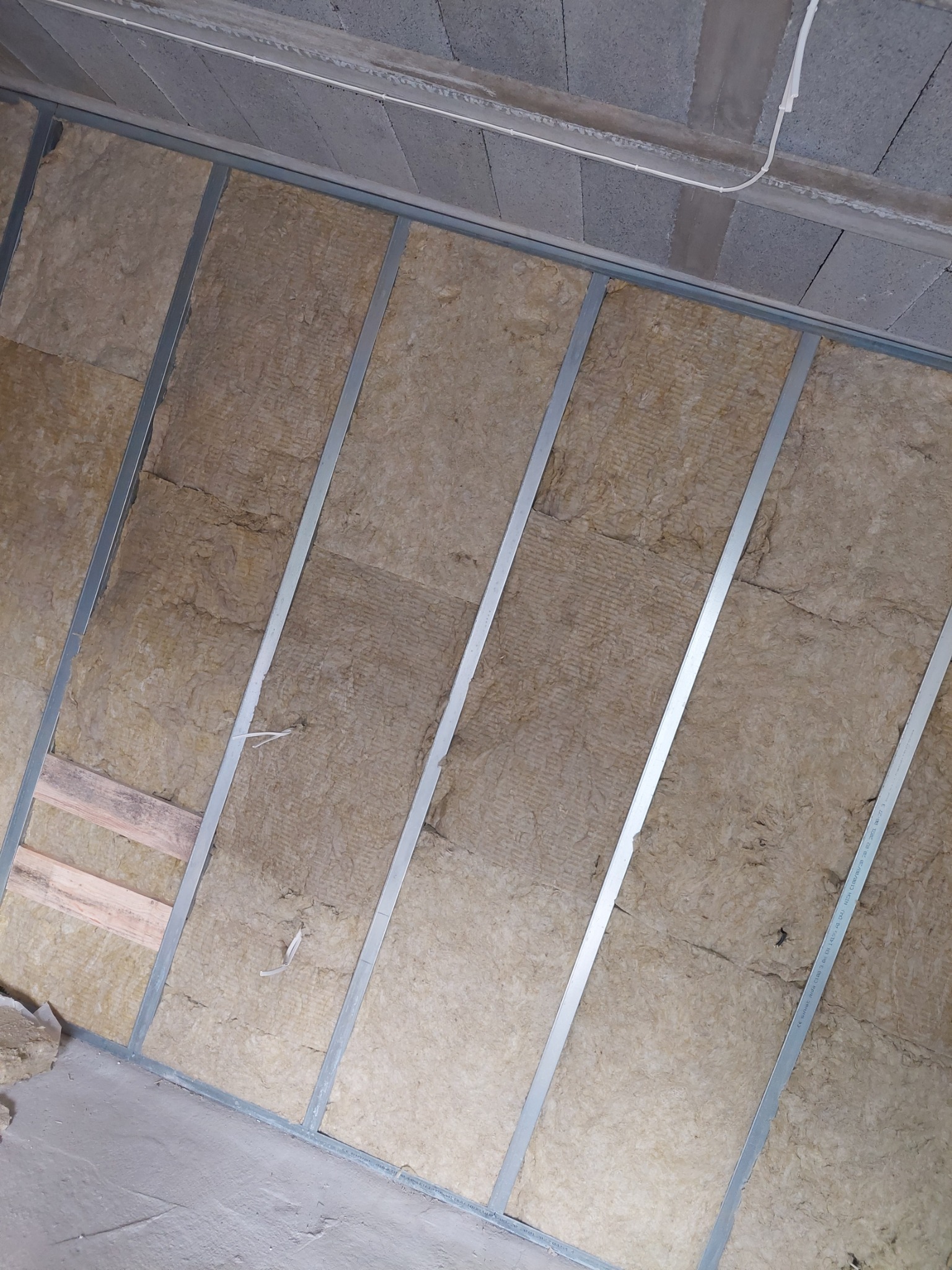 Montaż izolacji z wełny mineralnej w metalowym stelażu, widok na ścianę z bliska, fragment sufitu z betonu komórkowego.