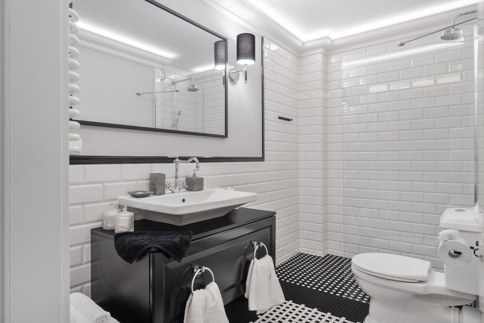 Biało-czarna łazienka z umywalką nablatową, baterią w stylu retro, lustrem w czarnej ramie, białymi płytkami typu metro i czarno-białą podłogą w szachownicę.