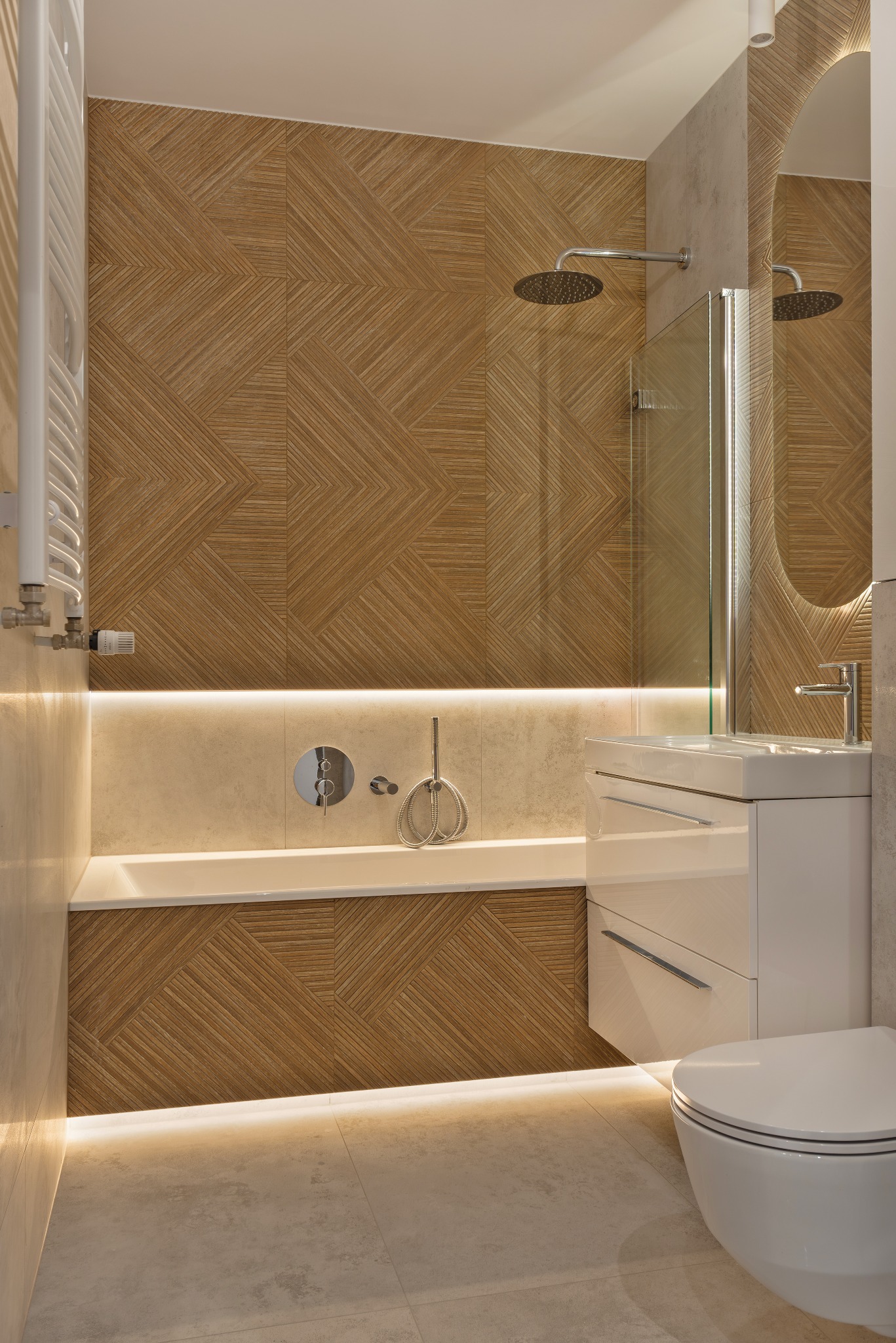Nowoczesna łazienka z drewnopodobnymi płytkami ułożonymi w geometryczny wzór na ścianach i obudowie wanny, podświetlona listwami LED, z białą umywalką i toaletą.