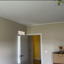 Michał Kromka - Jasne wnętrze po malowaniu: beżowe ściany, białe listwy, otwarte drzwi z widokiem na żółtą ścianę w tle. Minimalistyczny design i świeżość po remoncie.