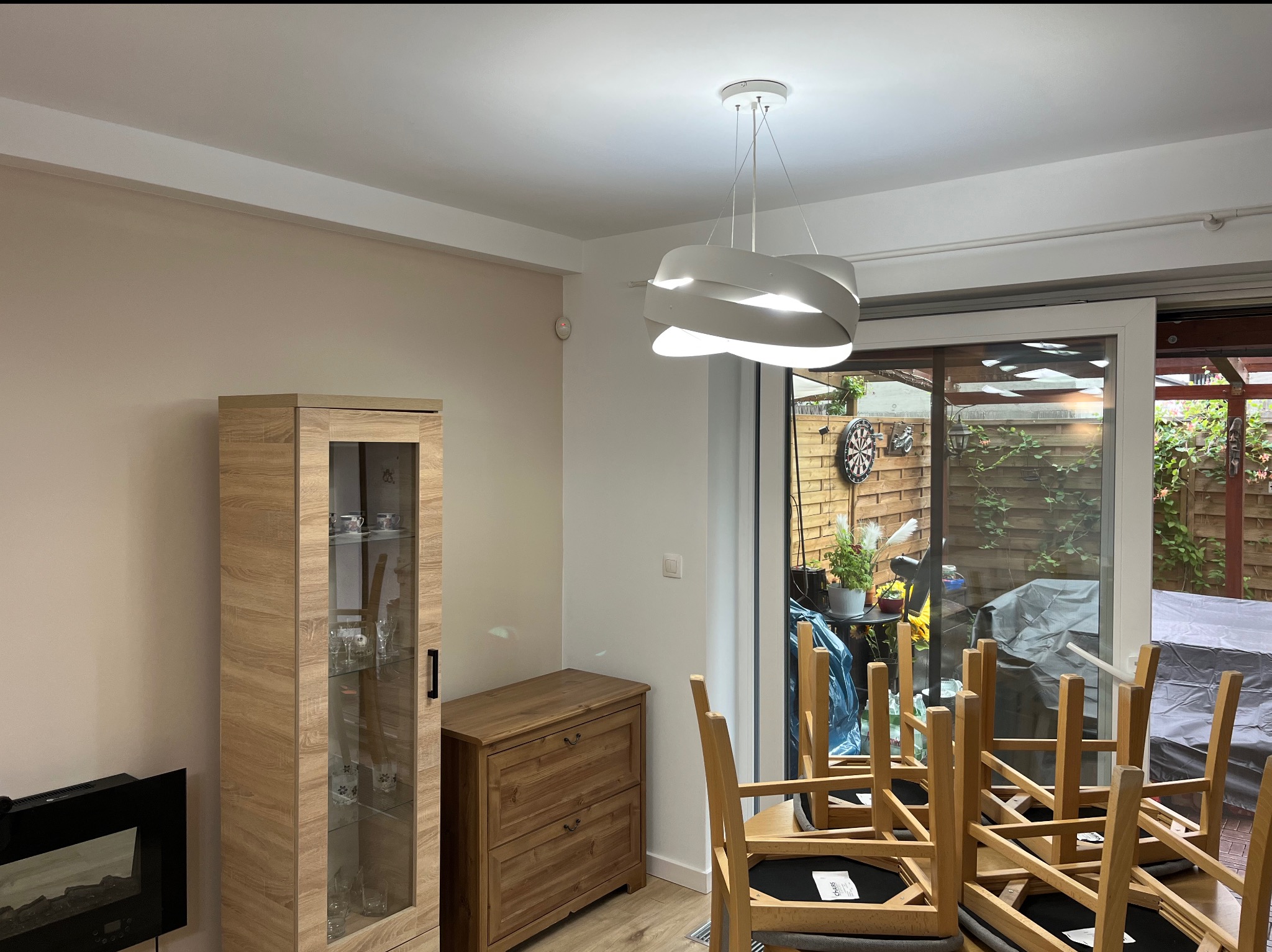 Jasne wnętrze z nowoczesną lampą wiszącą, drewnianymi meblami i krzesłami ustawionymi na stole, przygotowane do malowania ścian w odcieniu beżu.