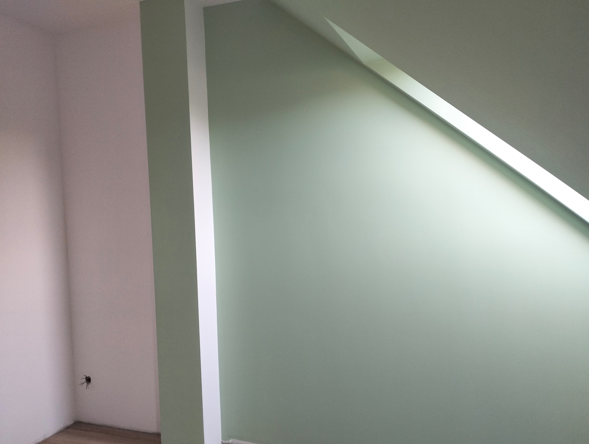 Świeżo pomalowane ściany w odcieniach zieleni i bieli w pokoju na poddaszu. Widoczny fragment podłogi i gniazdko elektryczne.