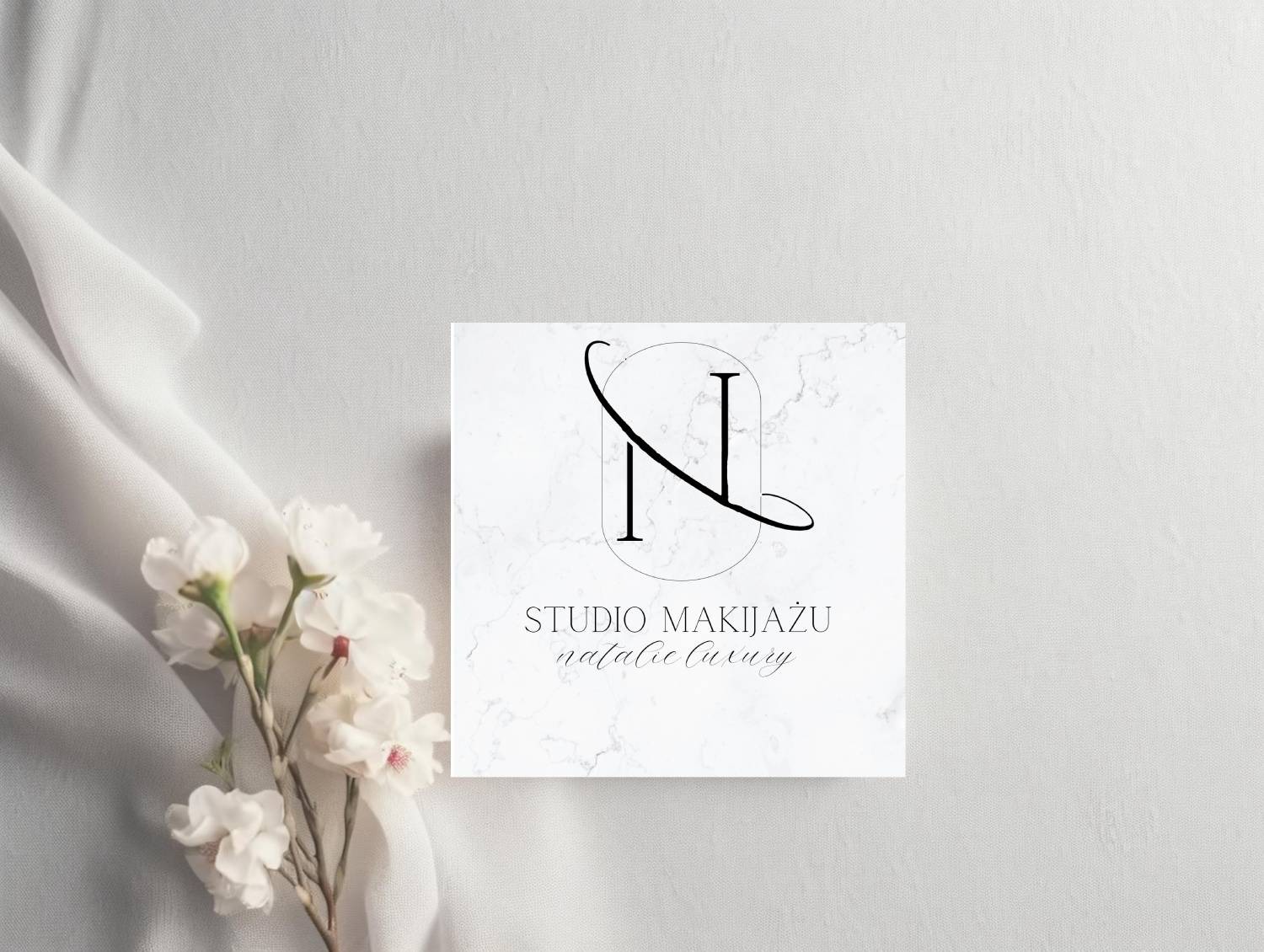 Eleganckie logo studia makijażu 'Natalie Luxury' na marmurowym tle, ozdobione białą tkaniną i delikatnymi kwiatami.
