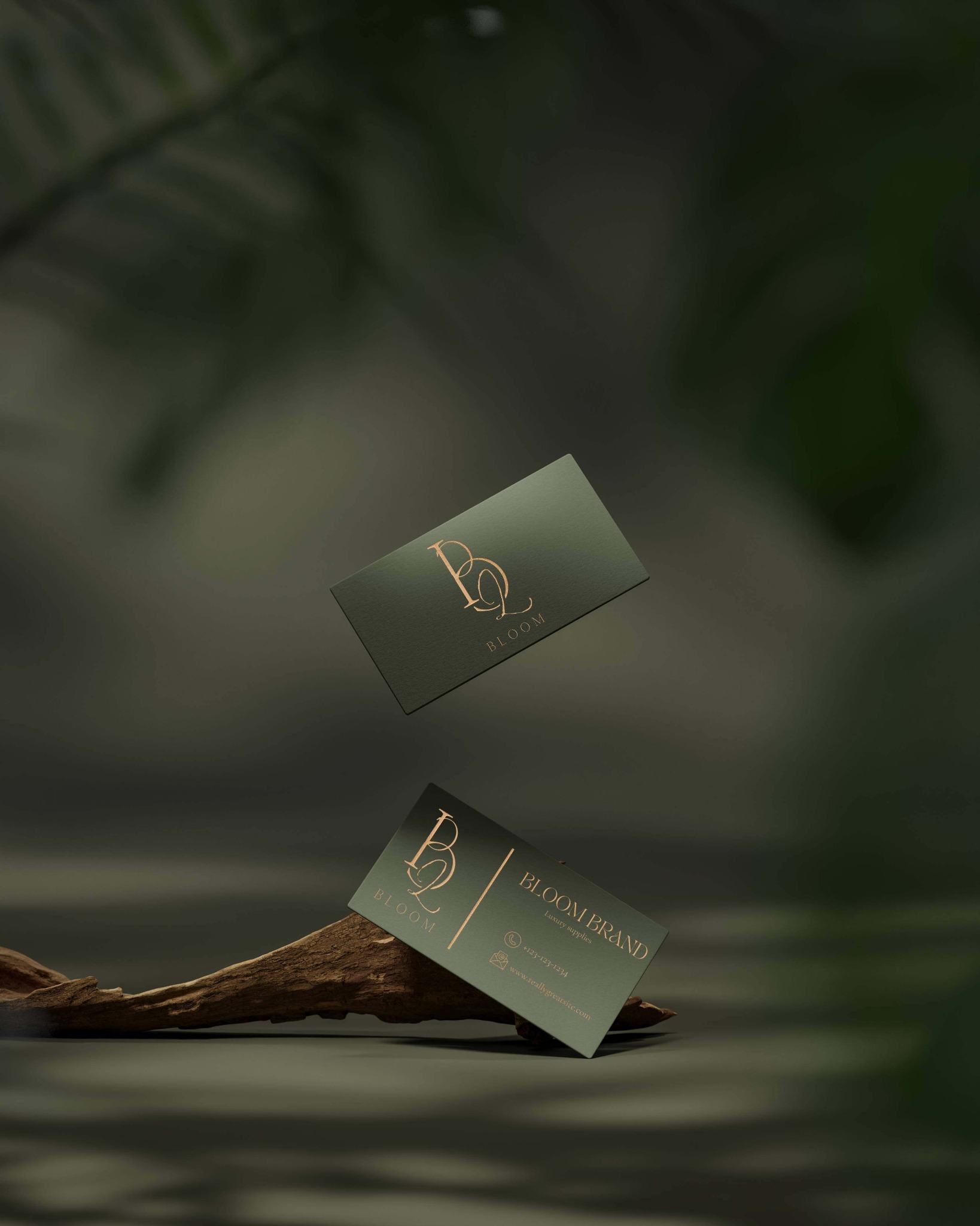 Dwie wizytówki marki Bloom na tle zieleni, jedna lewituje, druga oparta o kawałek drewna, złote logo i napisy na ciemnozielonym tle.