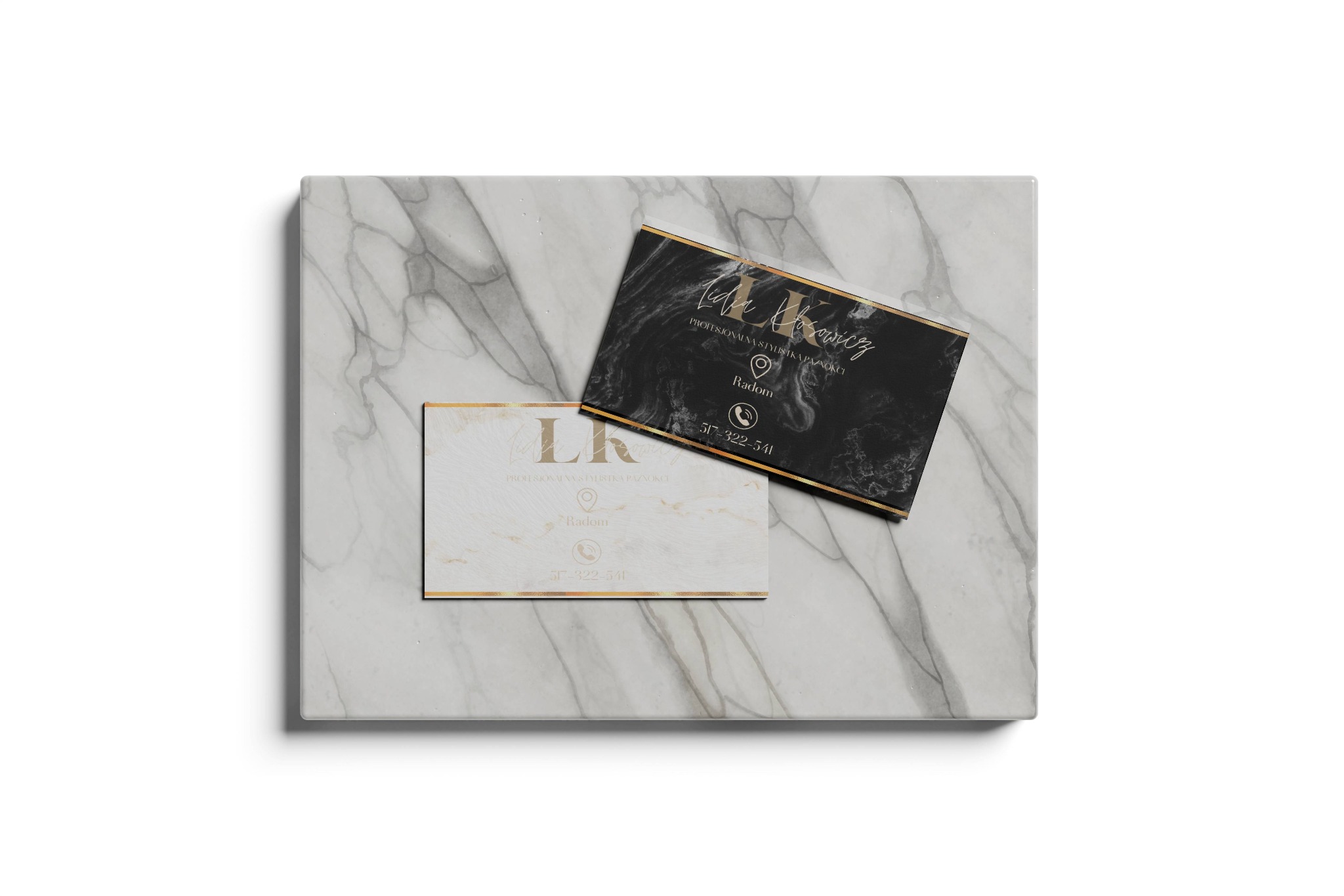Dwie wizytówki z marmurowym tłem, jedna biała z złotymi akcentami, druga czarna ze złotymi akcentami, leżące na marmurowej płycie.