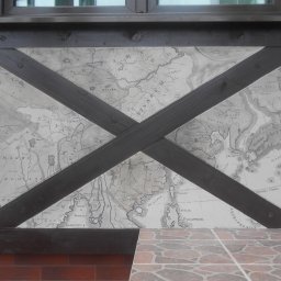 Olga Kananets - Fragment ściany z dekoracyjnym malowaniem przedstawiającym starą mapę Azji, przeciętej na skos drewnianymi belkami, widoczne fragmenty okna i płytek.