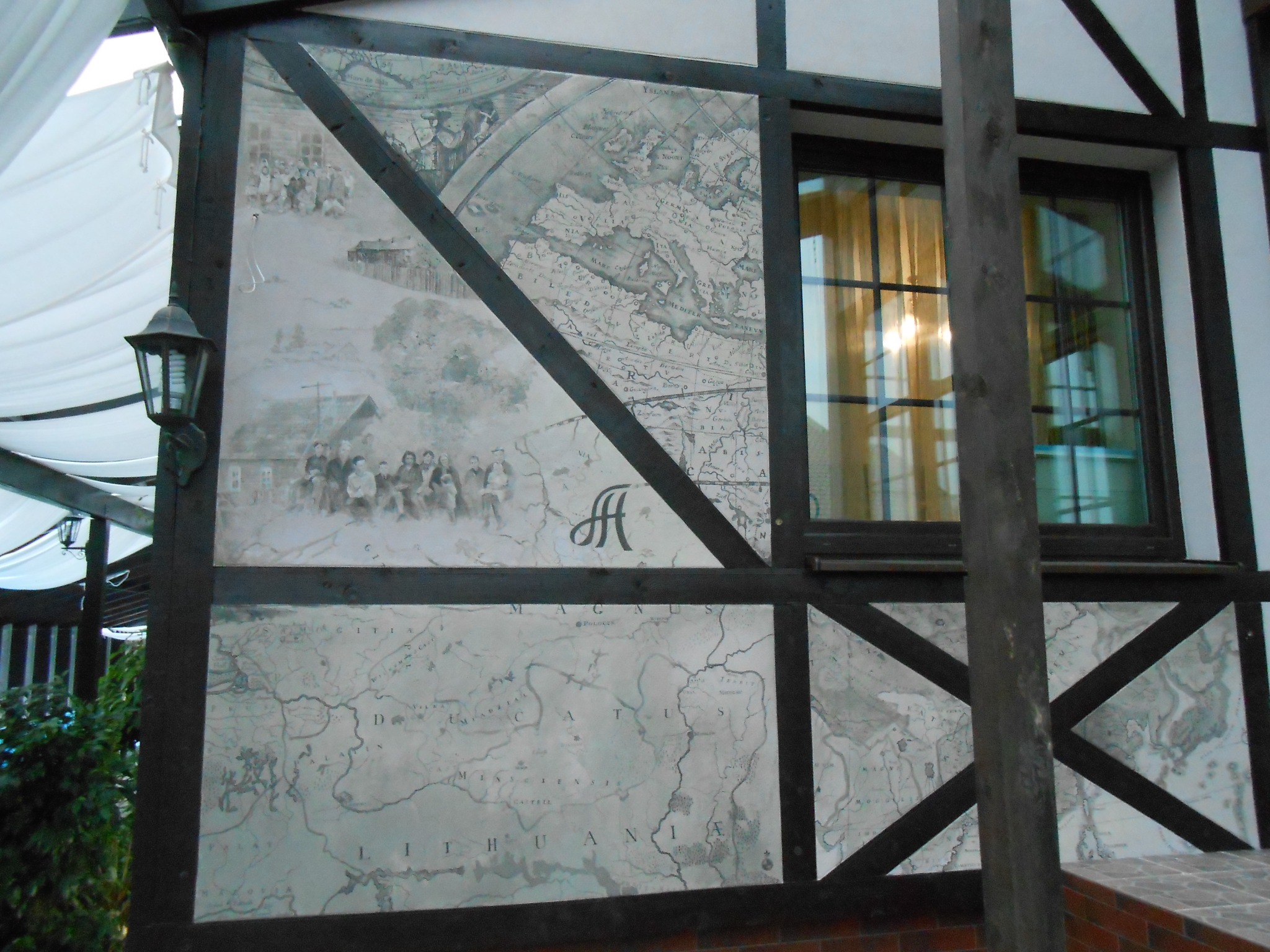 Fragment ściany w stylu szachulcowym z dekoracyjnym malowidłem przedstawiającym starą mapę Europy z elementami figuralnymi i ozdobnym monogramem.