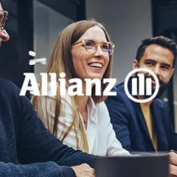 Grupa uśmiechniętych osób siedzi przy stole z laptopami, widoczne logo Allianz.