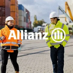 Dwie osoby w kaskach i odblaskowych kurtkach spacerują po placu budowy z kontenerami w tle, logo Allianz.