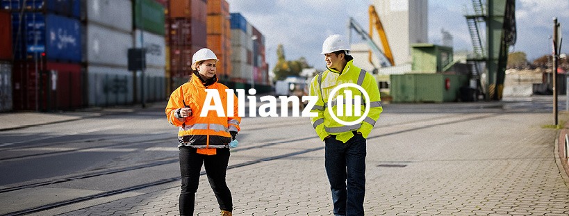 Dwie osoby w kaskach i odblaskowych kurtkach spacerują po placu budowy z kontenerami w tle, logo Allianz.