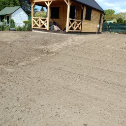 FHU EARTHWORKS AND GARDENING - Przygotowany teren pod trawnik z widocznymi śladami po maszynach, obok drewniany domek letniskowy i zielone ogrodzenie z siatki.