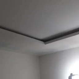 Wykończony sufit podwieszany z widoczną żarówką i śladami po łataniu na ścianie, w rogu pomieszczenia.