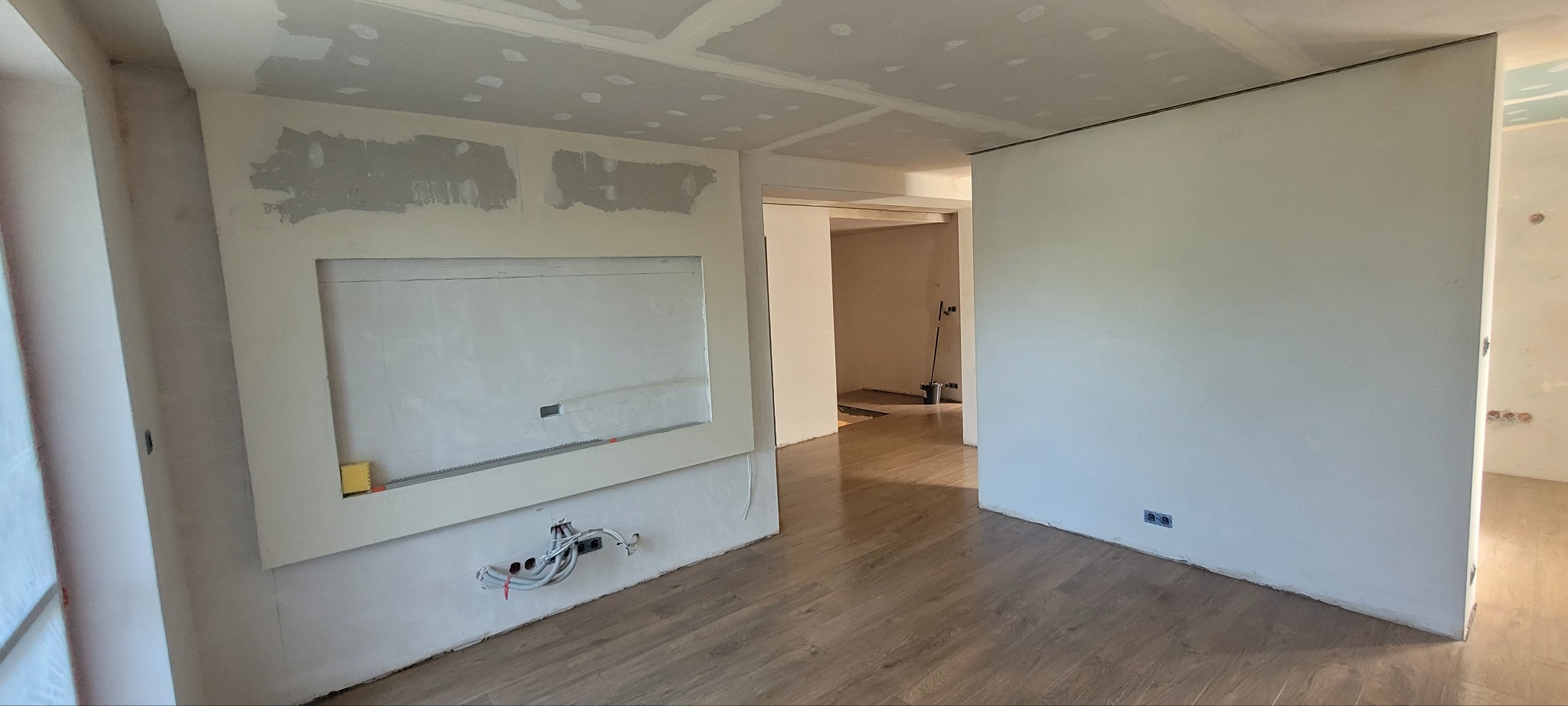 Wnętrze w trakcie prac wykończeniowych: ściany po szpachlowaniu, widoczne instalacje elektryczne, podłoga wyłożona panelami. Sufit z płyt gipsowo-kartonowych.