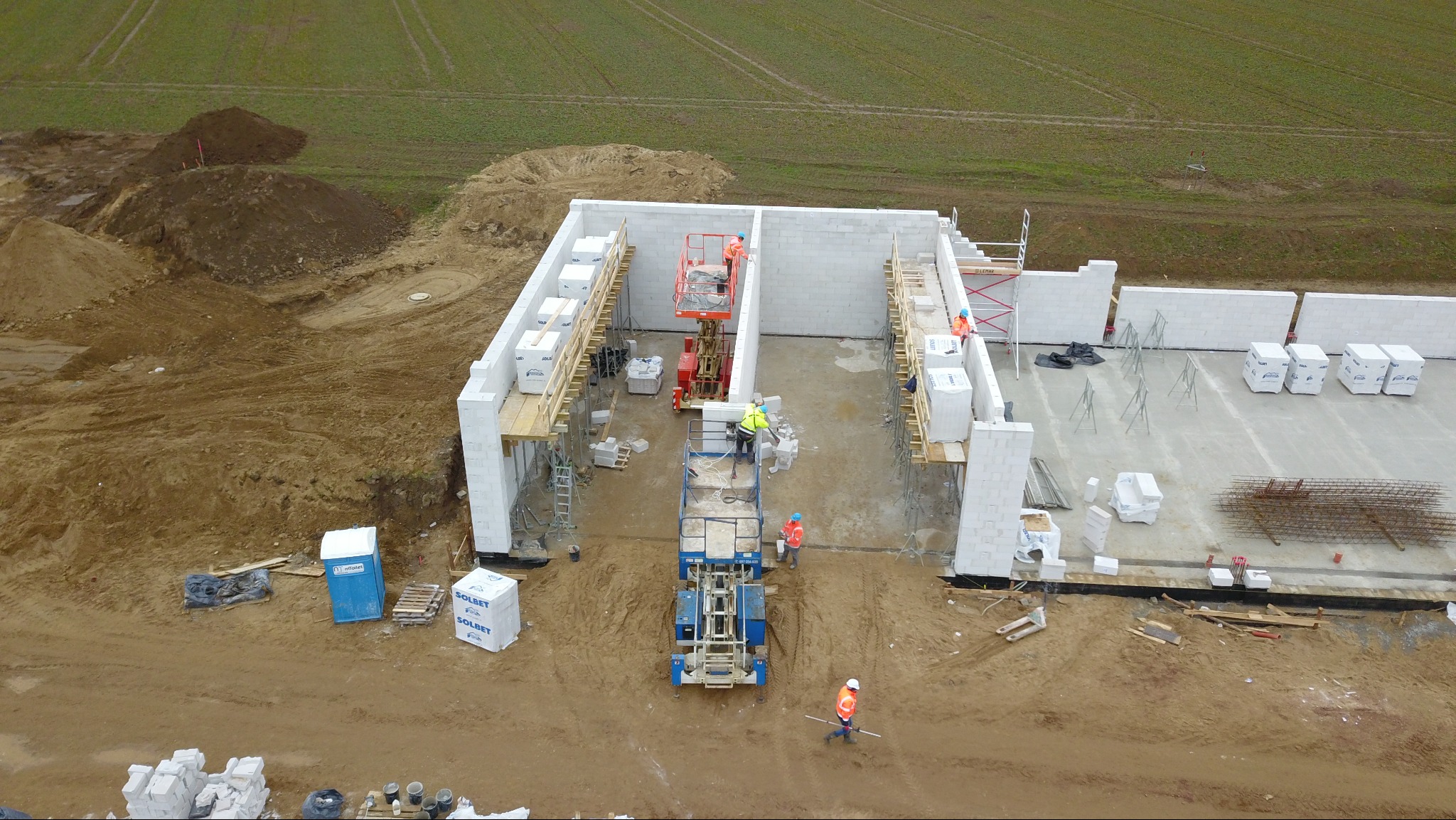 Budowa ścian z bloczków Solbet z użyciem podnośników i rusztowań. Widok z góry na plac budowy w trakcie prac murarskich.