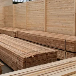 Stosy świeżo przetartego drewna ułożone w magazynie, zabezpieczone czarną taśmą, widoczne jasne słoje drewna i minimalne sęki.