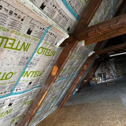 Builder Atta - Montaż membrany paroizolacyjnej Intello na drewnianej konstrukcji poddasza, widoczne krokwie i płyty OSB, taśma uszczelniająca na łączeniach, w tle drabiny i elementy wyposażenia.