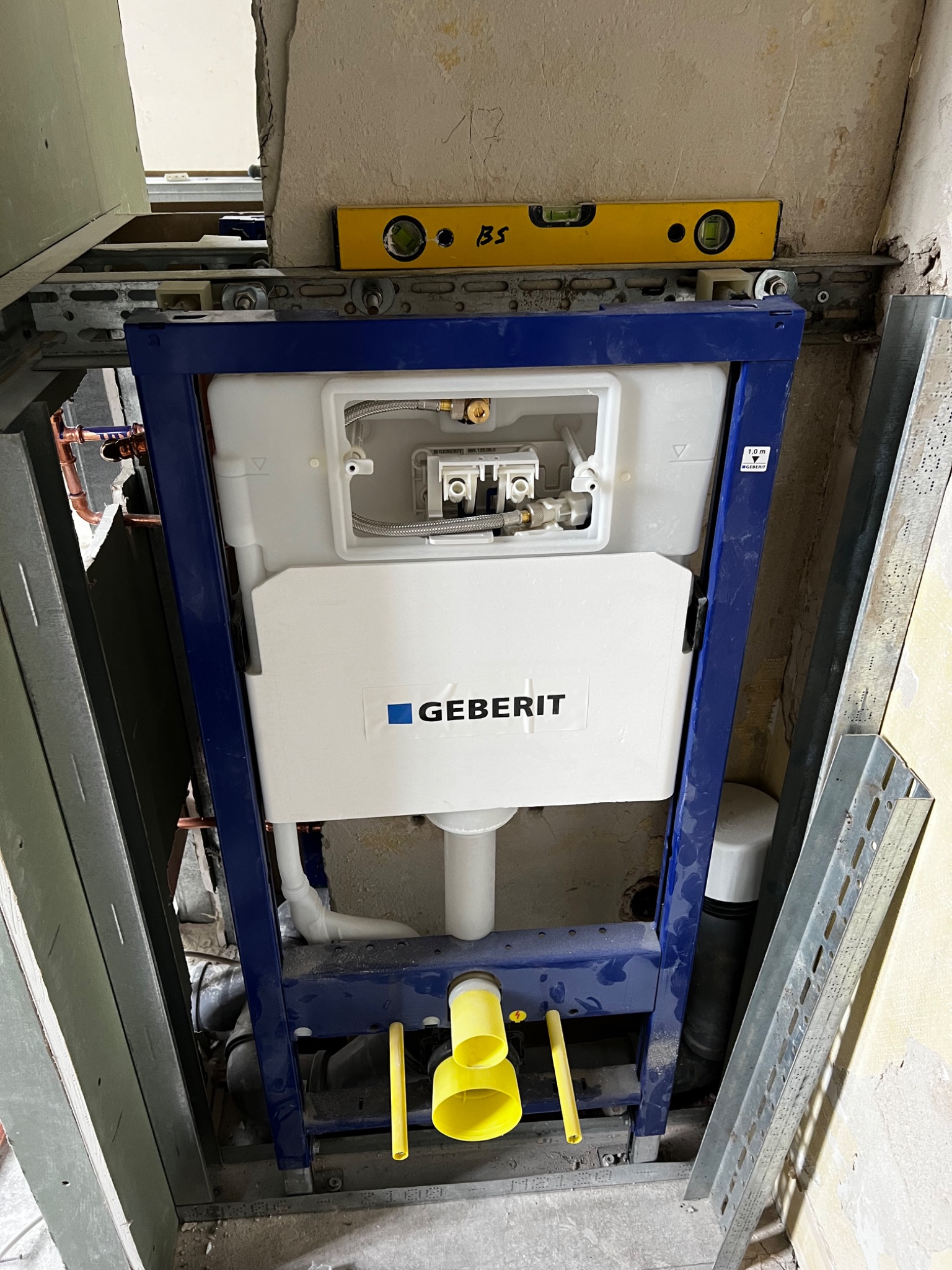 Stelaż podtynkowy Geberit zamontowany w trakcie remontu łazienki, poziomica na konstrukcji nośnej, widoczne rury i elementy instalacji.