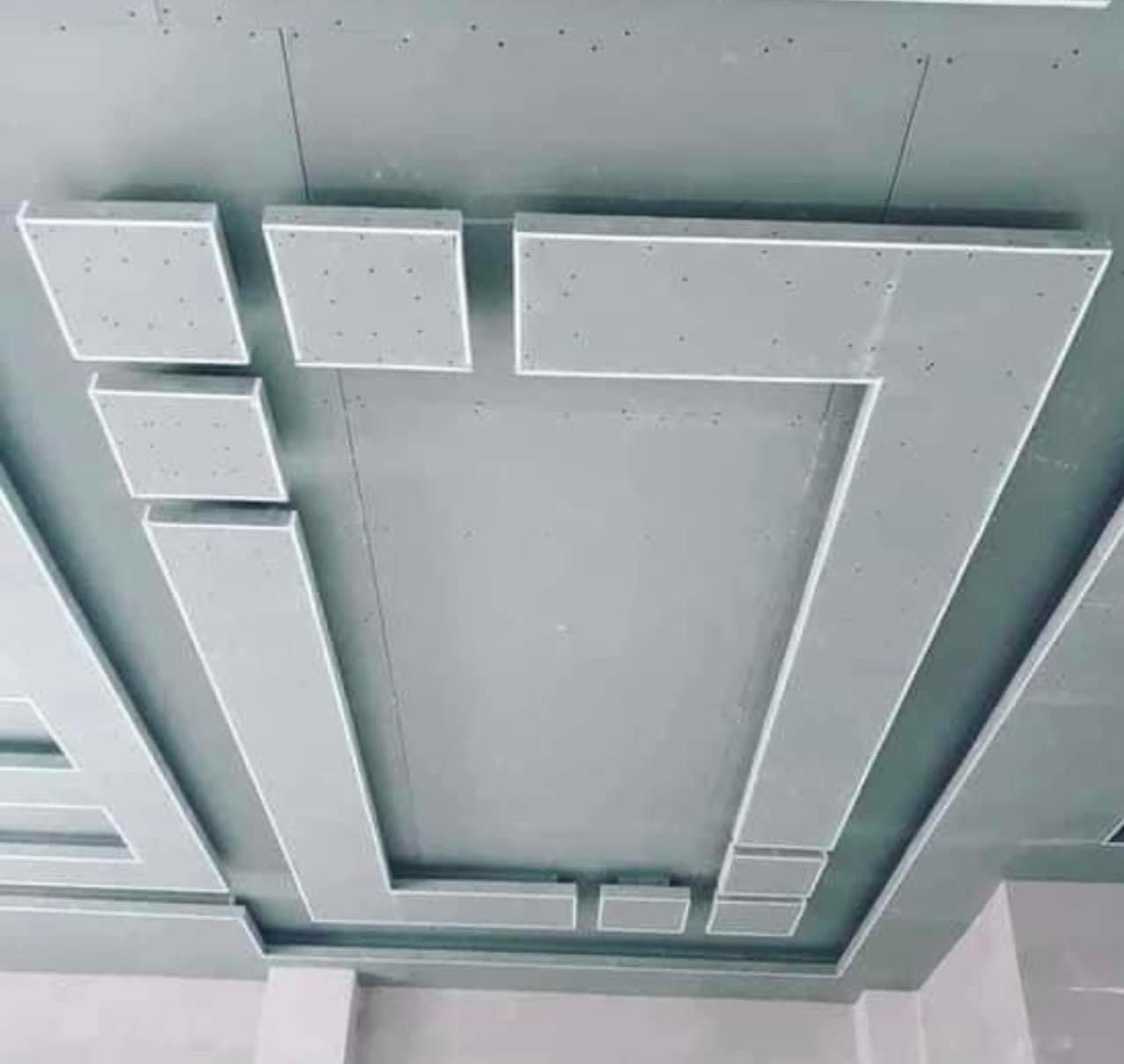 Sufit z płyt kartonowo-gipsowych, dekoracyjna konstrukcja z prostokątnych elementów i listew, widoczne ślady po szpachlowaniu, surowy stan wykończenia.