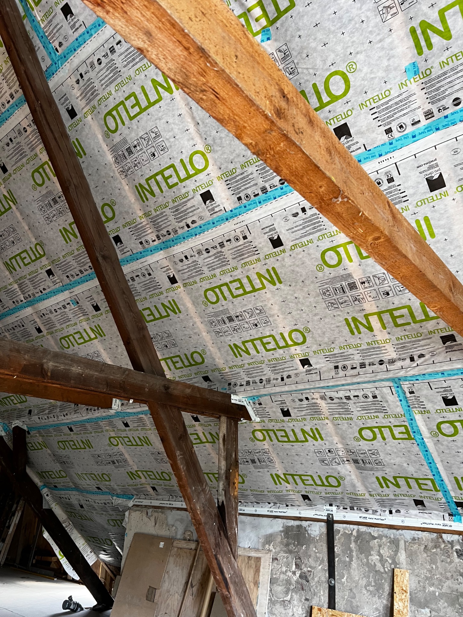 Widok poddasza z widoczną membraną paroizolacyjną Intello, zamontowaną między krokwiami drewnianymi, z widocznymi napisami i symbolami na membranie.