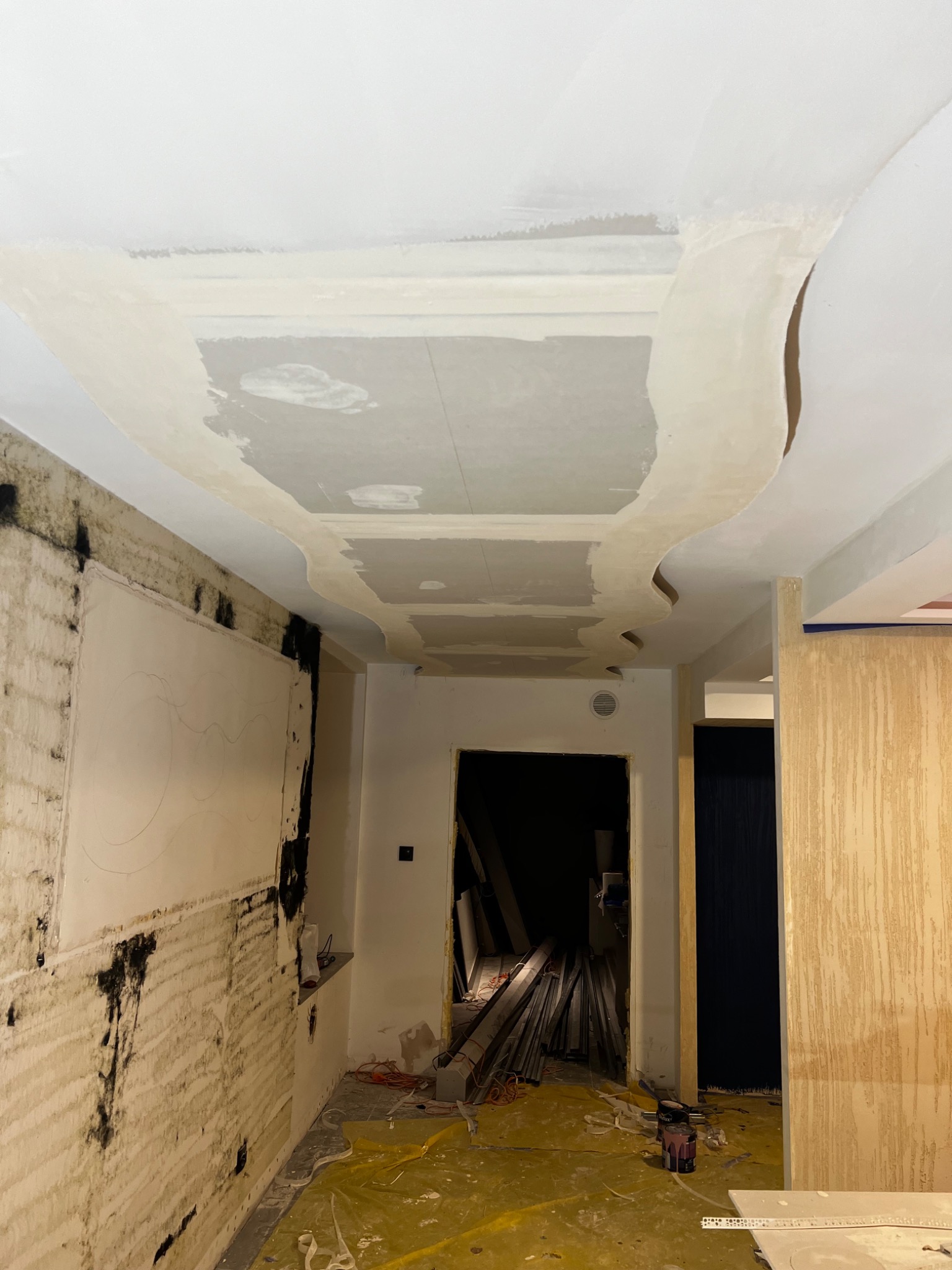 Wnętrze w trakcie remontu: fragment sufitu z dekoracyjnymi elementami przed nałożeniem gładzi, ściany z widocznymi śladami przygotowania podłoża, zabezpieczona folią podłoga oraz widoczne narzędzia...