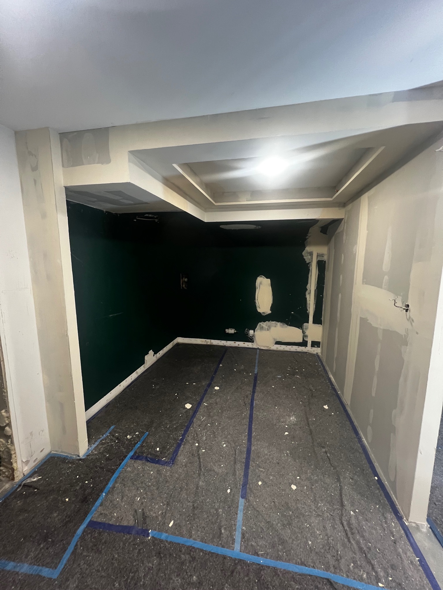 Pokój w trakcie prac wykończeniowych: ściany pokryte szpachlą, zabezpieczona podłoga, widoczny fragment sufitu podwieszanego z dekoracyjnym wykończeniem.