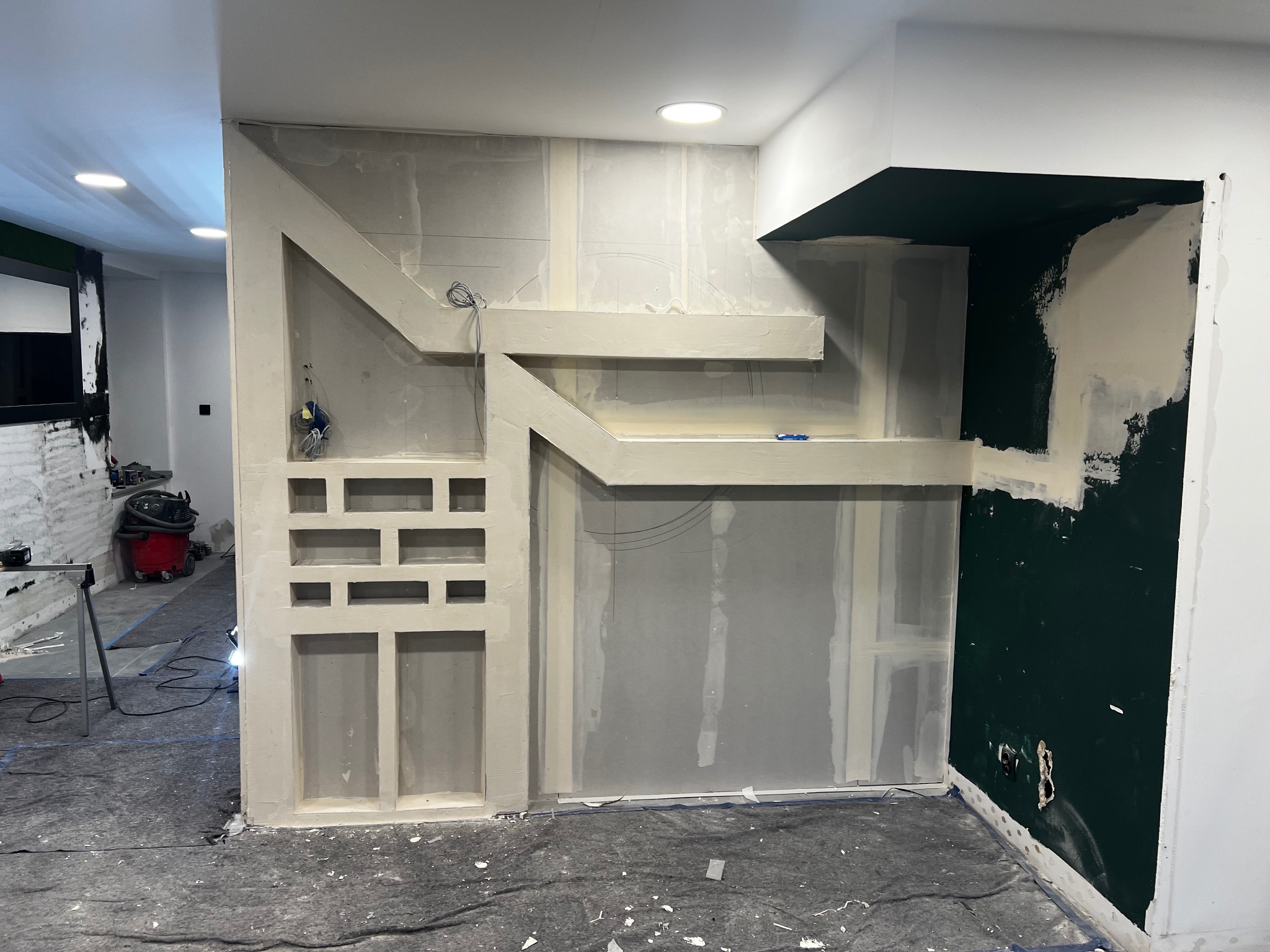 Ściana z płyty karton gips z elementami dekoracyjnymi w trakcie montażu, widoczne przewody elektryczne i częściowo pomalowana ściana w ciemnym kolorze