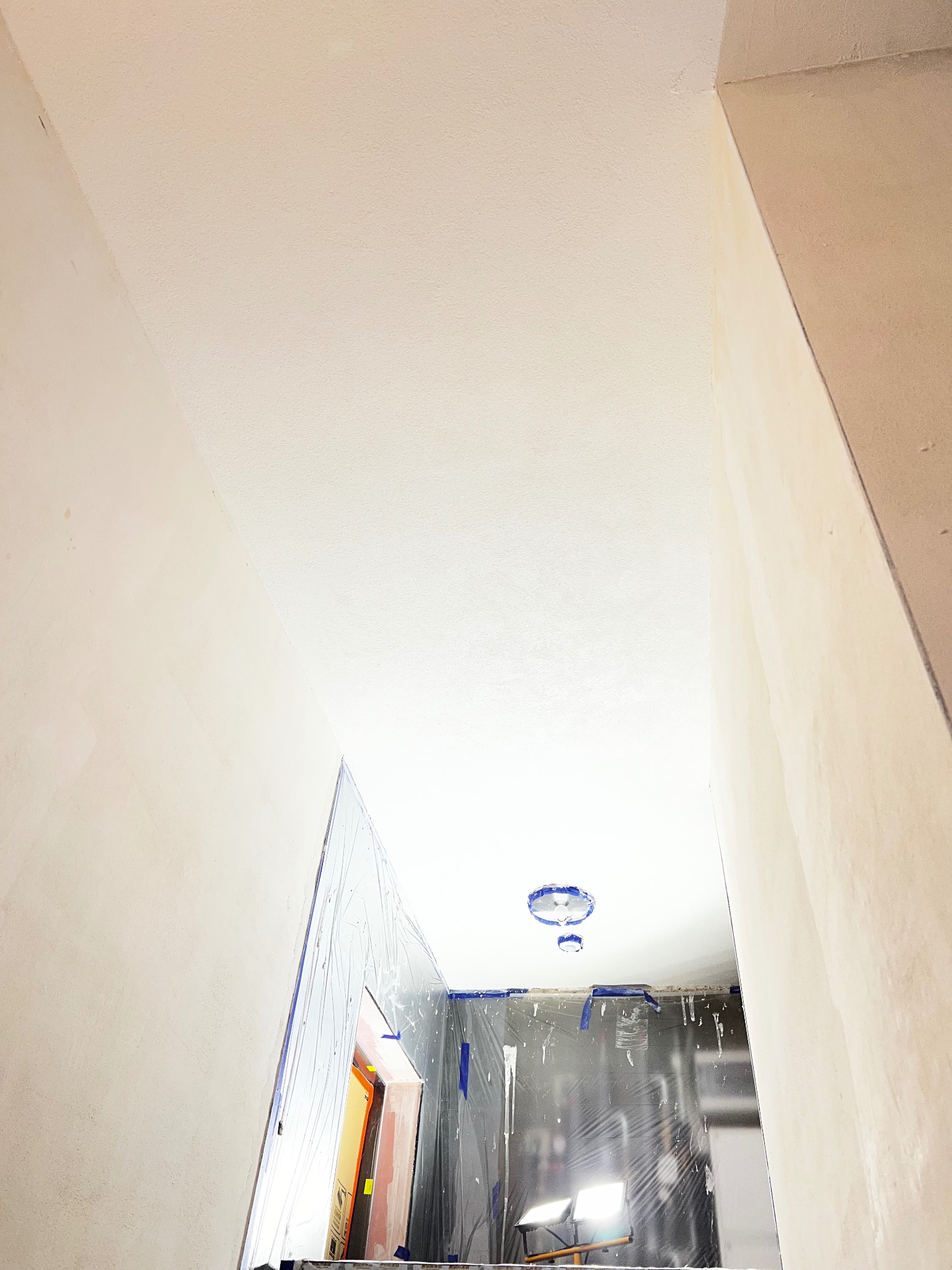 Wnętrze po gładziowaniu: świeżo wygładzone ściany i sufit w jasnym odcieniu, zabezpieczone folią elementy, widoczne lampy oświetlające przestrzeń.