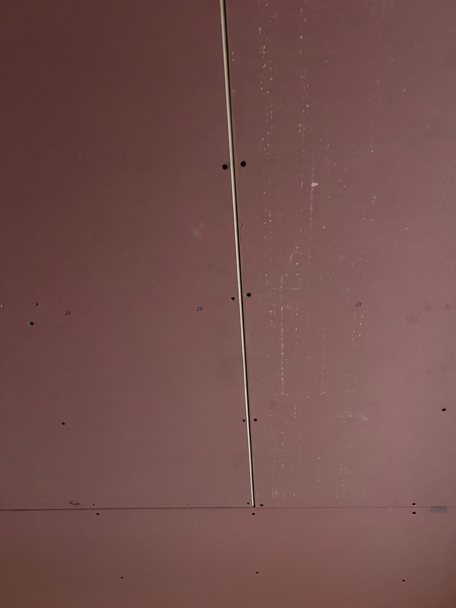 Montaż płyt karton-gips na suficie, widoczne łączenia i ślady po wkrętach. Czerwonawe płyty, surowy stan przed wykończeniem.