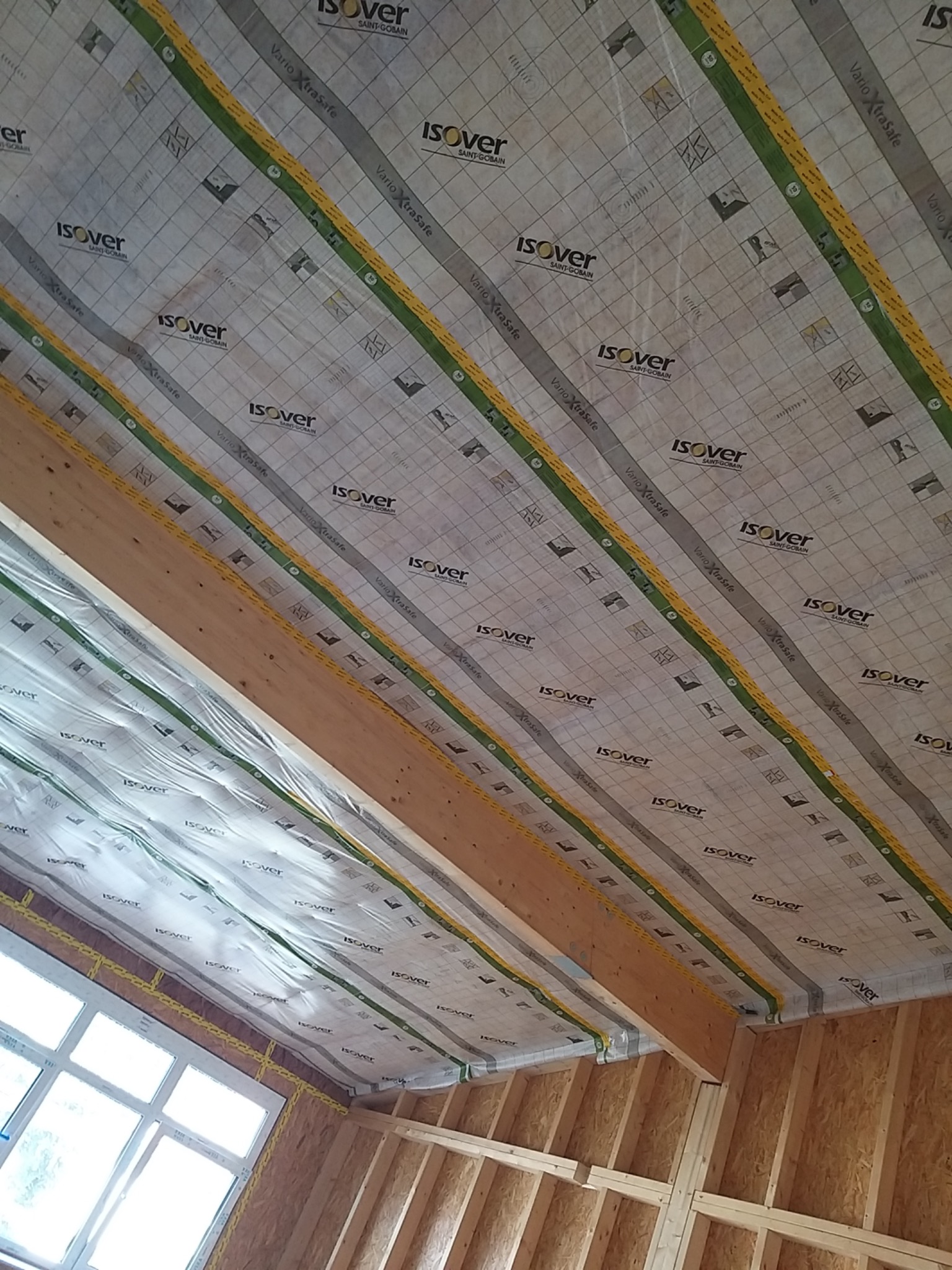 Ocieplenie poddasza folią paroizolacyjną Isover Vario XtraSafe, widok na drewnianą konstrukcję dachu i okno w Koszalinie.