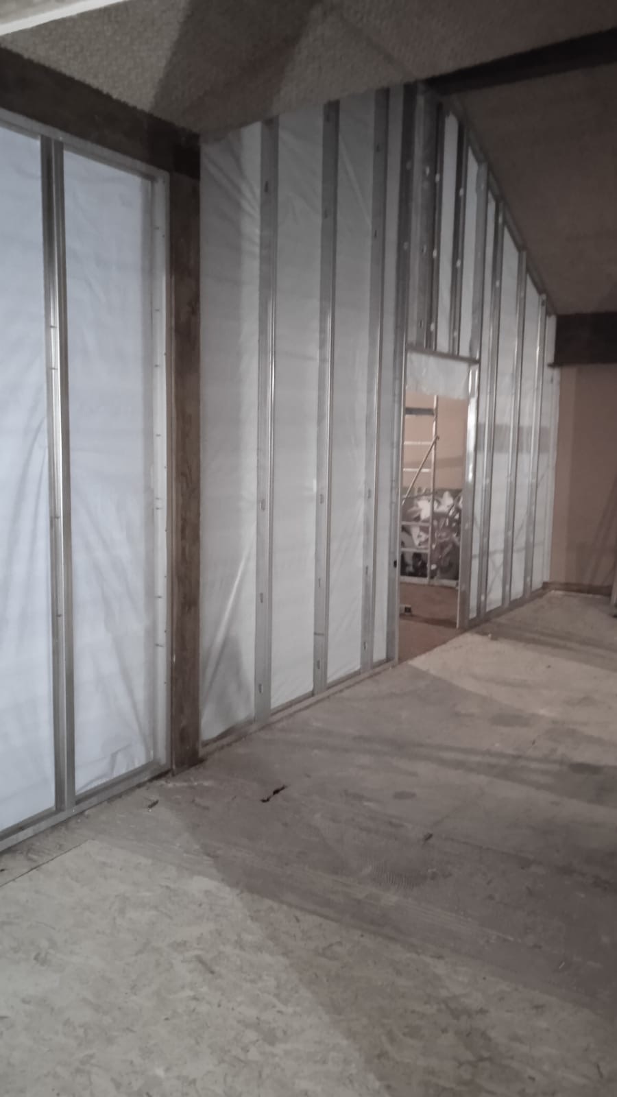 Metalowy szkielet ścian działowych z płyt karton-gips, widoczne profile i białe wypełnienie, surowy betonowy sufit i podłoga, w tle drabina.