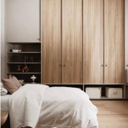 PKN Estate Sp. z o.o. - Sypialnia z dużą szafą przesuwną o drewnianych frontach, wbudowaną w ścianę. Po lewej stronie szafy wnęka z półkami i dekoracjami. Na podłodze drewniany parkiet.
