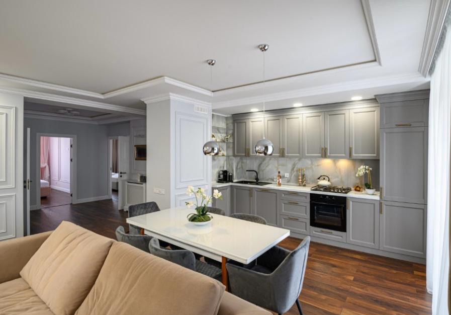 Elegancka kuchnia w szarościach z marmurowym backsplashiem i drewnianą podłogą. Widok z salonu na stół jadalny i zabudowę kuchenną z oświetleniem punktowym.