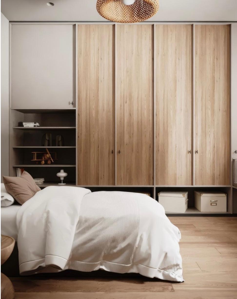Sypialnia z dużą szafą przesuwną o drewnianych frontach, wbudowaną w ścianę. Po lewej stronie szafy wnęka z półkami i dekoracjami. Na podłodze drewniany parkiet.