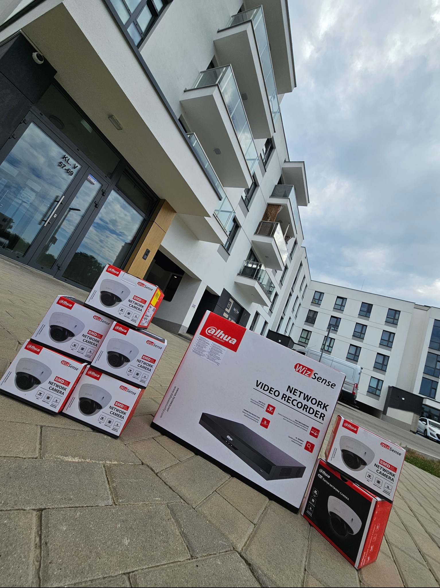 Pudełka z kamerami i rejestratorem Dahua WizSense przed nowoczesnym budynkiem mieszkalnym. Sprzęt do monitoringu wizyjnego.
