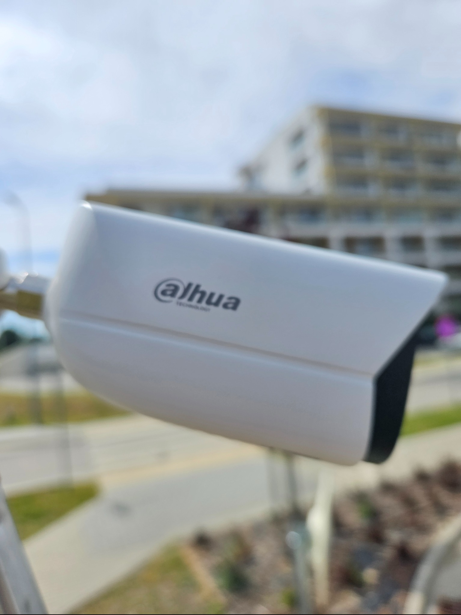 Kamera monitoringu Dahua na tle budynku i nieba. Widoczny fragment chodnika i ulicy. Kamera zamontowana na zewnątrz, skierowana w stronę ulicy.
