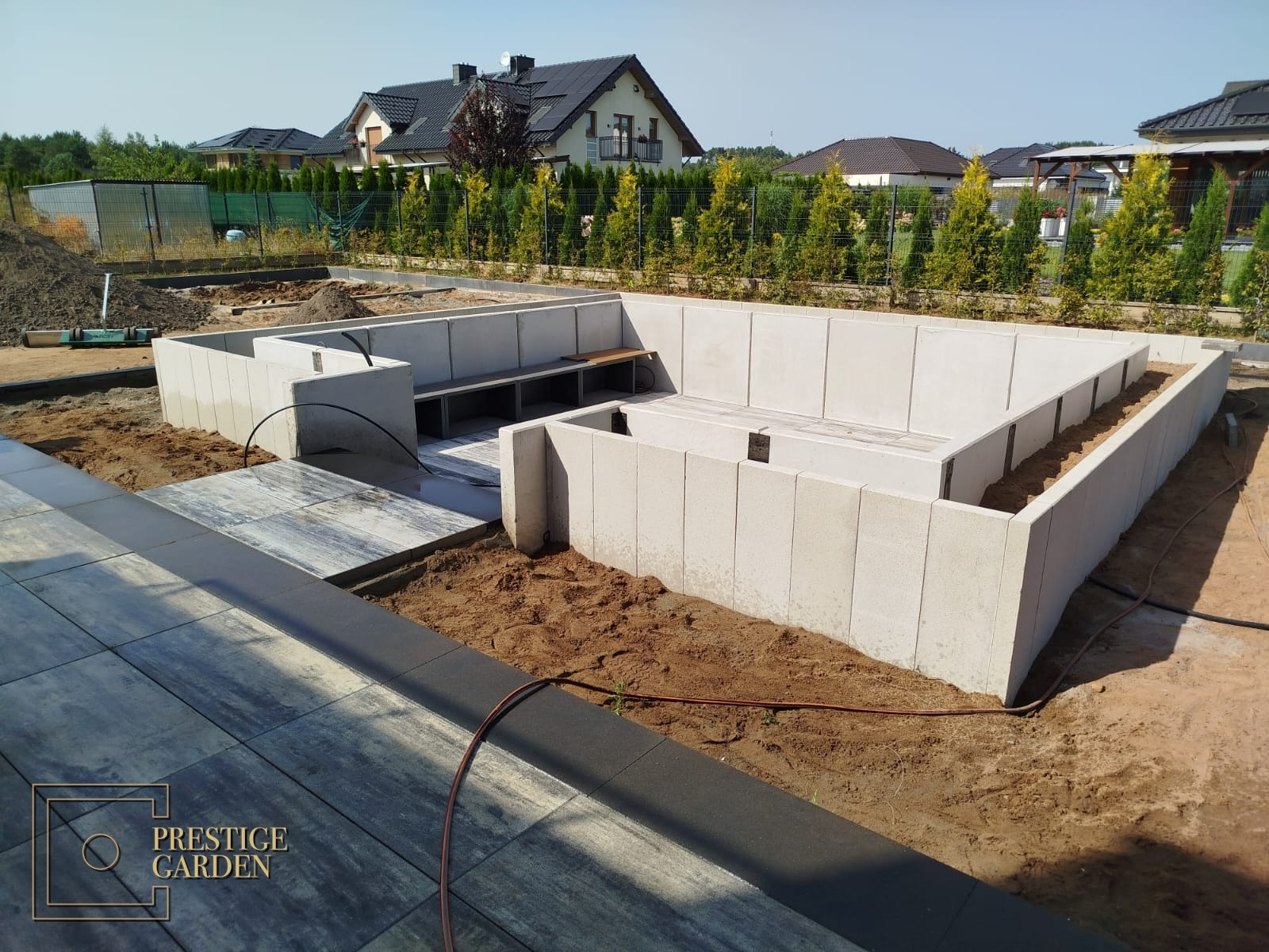 Fundamenty betonowe pod budowę elementu wodnego w ogrodzie, widoczne także ułożone płyty chodnikowe i przygotowane podłoże.