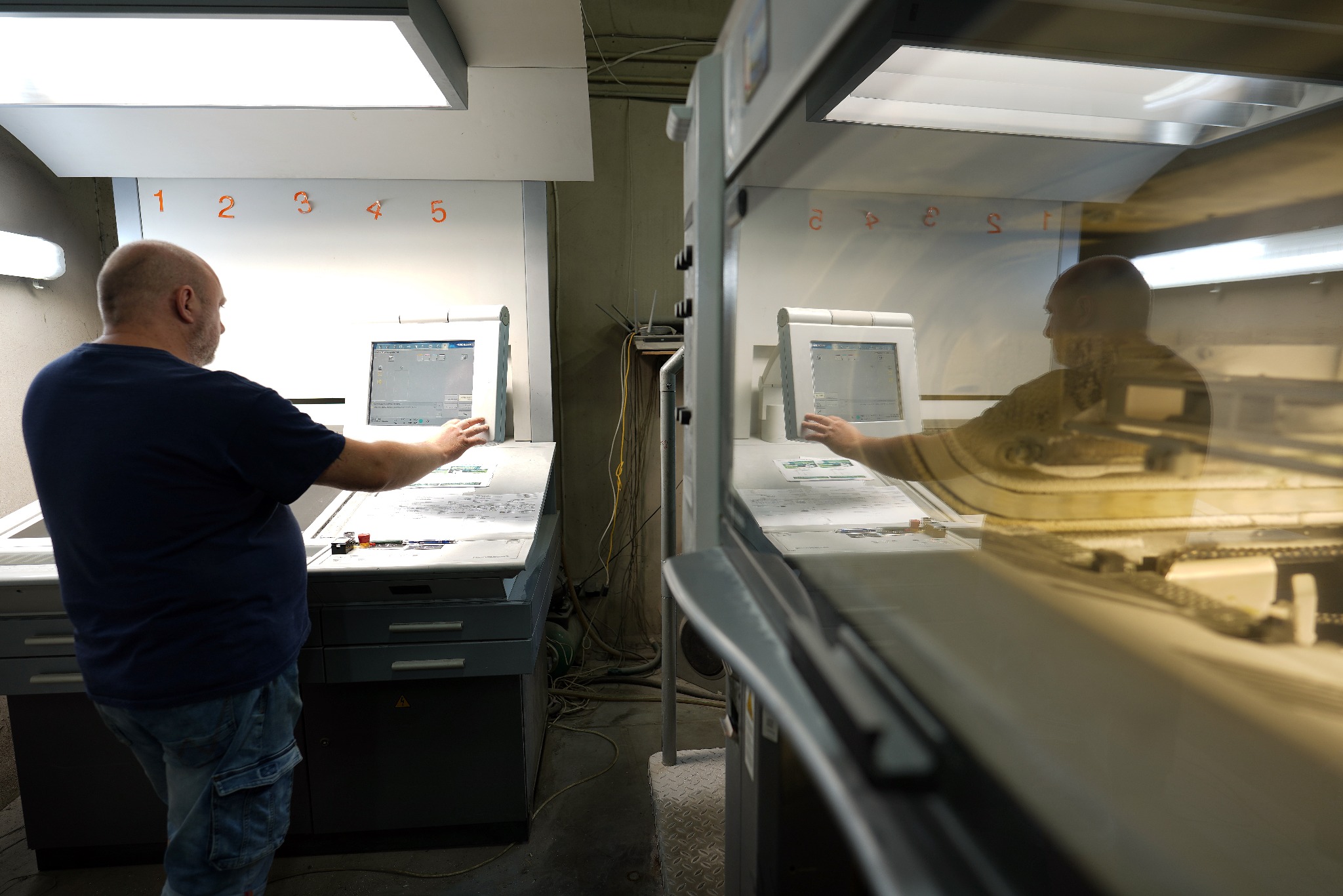 Operator obsługuje maszynę CTP (Computer-to-Plate) w drukarni, przygotowując płyty do druku offsetowego; widoczne numery 1-5 nad stanowiskiem pracy.